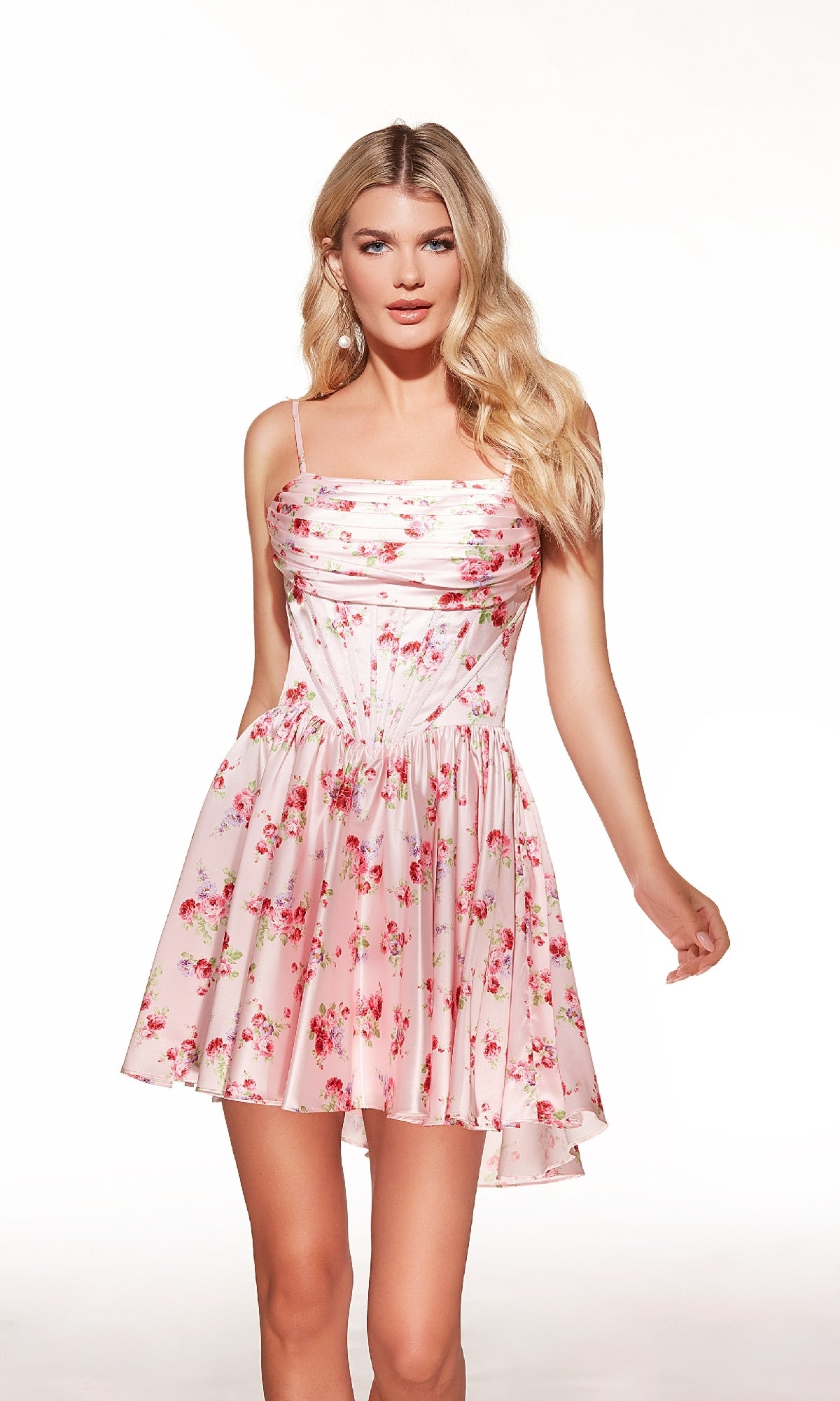A woman wears the Lace-Up Short Print Hoco Dress: Alyce 30059, a light pink floral homecoming dress featuring a slightly flared skirt and lace-up back, standing against a plain white background.